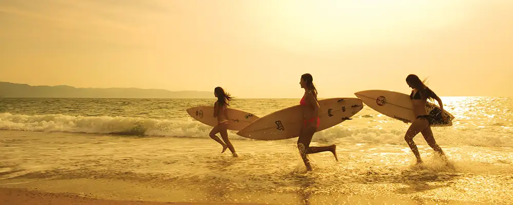 Three surfer girls running along a beach (c)Hyatt