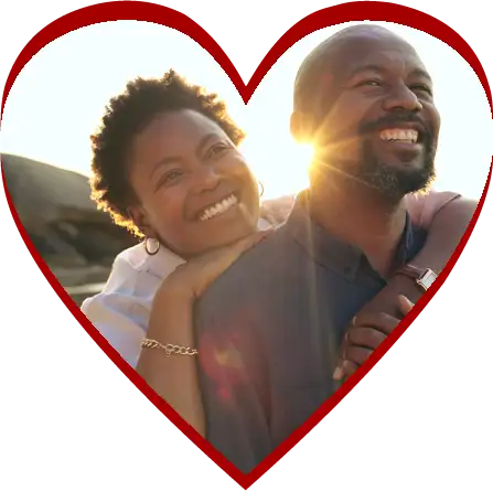 A middle aged couple embraces on the beach, smiling, in a heart-shape