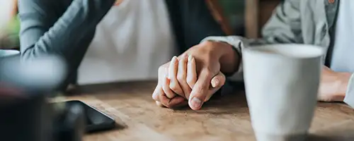 A couple holding hands with a phone on the table